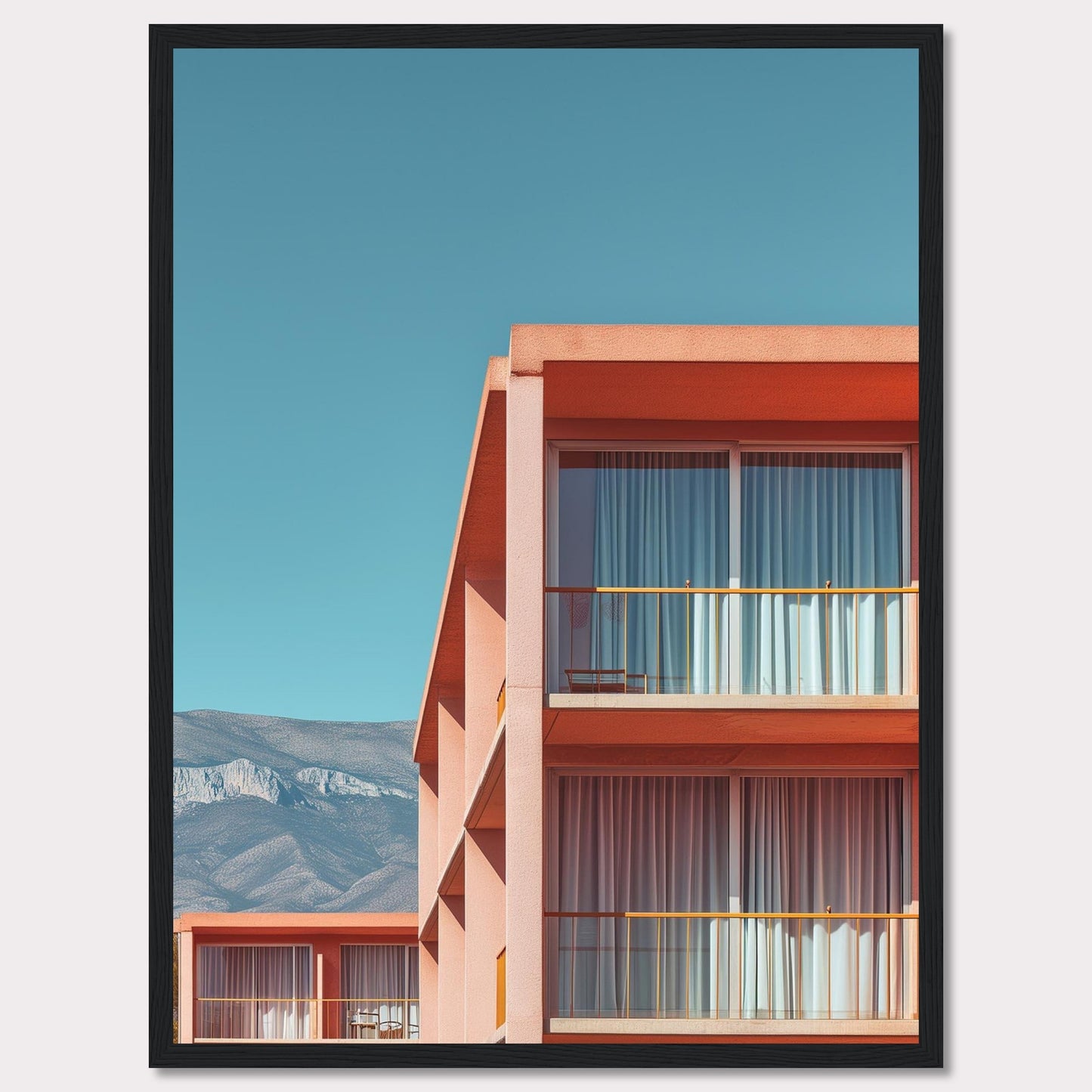 This captivating image showcases a modern building with a vibrant orange facade under a clear blue sky. The structure features large glass windows with white curtains, and balconies equipped with minimalistic furniture. In the background, majestic mountains add a serene touch to the scene.