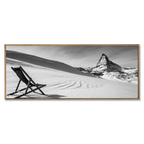 Framed black and white artwork of a mountain and chair on a snowy landscape.
