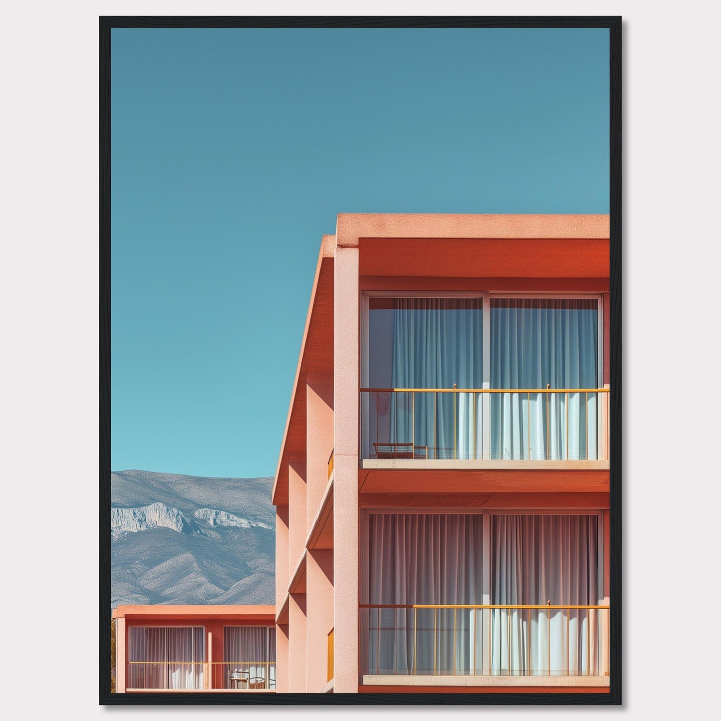 This captivating image showcases a modern building with a vibrant orange facade under a clear blue sky. The structure features large glass windows with white curtains, and balconies equipped with minimalistic furniture. In the background, majestic mountains add a serene touch to the scene.