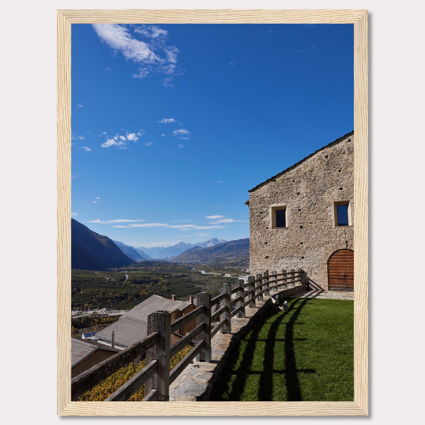 This stunning photograph captures a serene mountain landscape under a clear blue sky. The image features a rustic stone building with wooden windows and an arched wooden door. A wooden fence runs along the green grass, casting shadows that add depth to the scene. In the distance, majestic mountains stretch out, creating a breathtaking view.